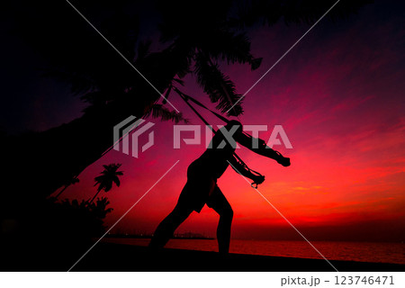 The athlete performs exercises on the beach with fitness straps 123746471