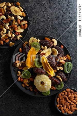 Dried tropical fruits, nuts, and raisins in black plate. Dried tropical fruits, nuts, and raisins in black plate. 123747847