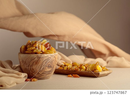 Yellow sultana raisins in a wooden bowl on a beige background. 123747867