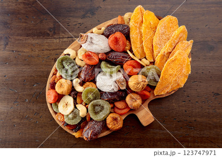 Dried mango slices, tropical fruits, nuts, and raisins on an old wooden table. Dried mango slices, tropical fruits, nuts, and raisins on an old wooden table. 123747971