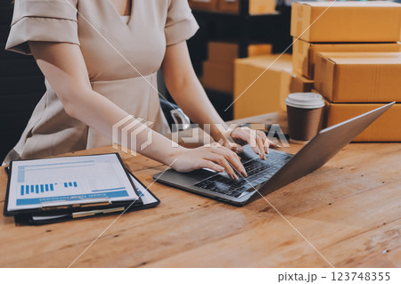 Startup SME small business entrepreneur of freelance Asian woman using a laptop with box Cheerful success Asian woman her hand lifts up online marketing packaging box and delivery SME idea concept 123748355