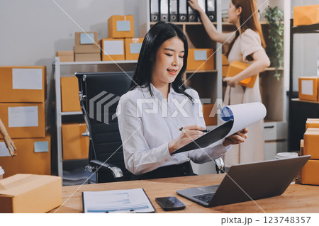 Startup SME small business entrepreneur of freelance Asian woman using a laptop with box Cheerful success Asian woman her hand lifts up online marketing packaging box and delivery SME idea concept 123748357