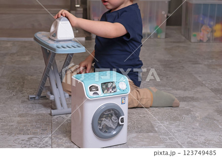 Little boy plays with toy iron and washing machine at home on floor. Cleaning, household chores, kids and educational games.  123749485