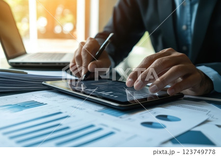 Professional man analyzing data on a tablet device while surrounded by charts and graphs representing business growth and financial performance in a modern office setting 123749778