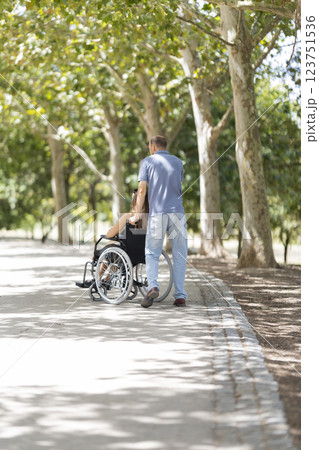 Man pushing woman in wheelchair along path in park 123751536