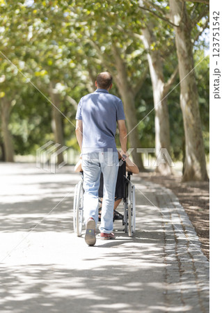 Nurse pushing senior woman in wheelchair along path in park 123751542