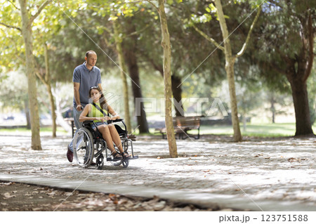 Man pushing woman in wheelchair in park during sunny day 123751588