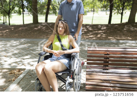 Man pushing sad disabled woman in wheelchair in park 123751656