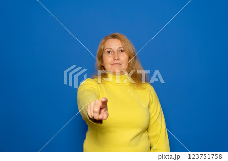 Caucasian woman in her 40s wearing a yellow sweater pointing at the camera while smiling in a positive attitude, isolated over blue studio background. 123751758
