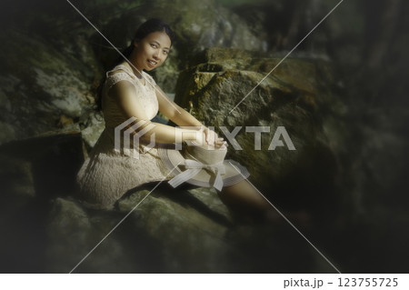 Indonesian girl in a dress sitting on the rocks Indonesian girl in a dress sitting on the rocks 123755725