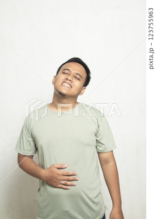 Fat Asian man with brown skin feels stomach ache with pain and his hand is holding his stomach, digestive health concept Fat Asian man with brown skin feels stomach ache with pain and his hand is holding his stomach, digestive health concept 123755963