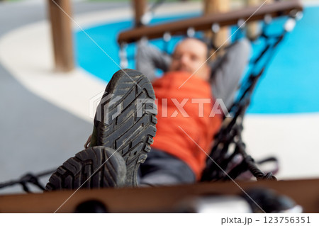 Close-up of rugged hiking boot sole in focus, with blurred man relaxing in hammock at an outdoor playground, concept for relaxation, adventure, and outdoor recreation themes 123756351