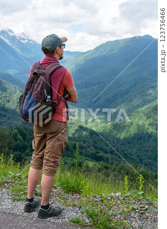 man traveler with backpack looking breathtaking mountain landscape Wearing green cap , red shirt, looks over green hills , peaks under cloudy sky. outdoor adventure, beauty of nature Hiking man traveler with backpack looking breathtaking mountain landscape Wearing green cap , red shirt, looks over green hills , peaks under cloudy sky. outdoor adventure, beauty of nature Hiking 123756466