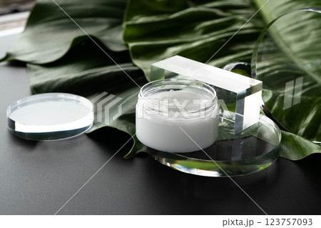 A cream container rests elegantly on a green leaf, amidst glass elements in a spa. 123757093