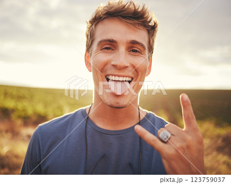Man, hands and portrait of rock sign for travel tour or vacation in the countryside and nature outdoors. Happy, excited young male traveler, rocker or musician with hand gesture and tongue out 123759037