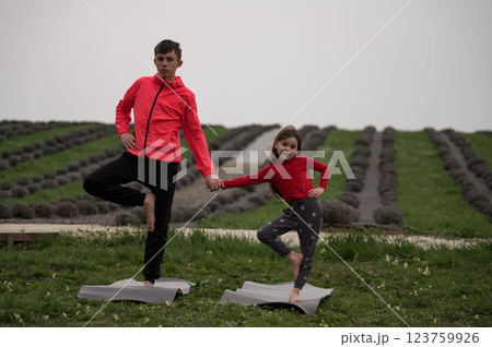 Siblings practicing yoga poses in a lavender field during a serene afternoon, enjoying nature while strengthening their bond and balance amid blooming flowers 123759926