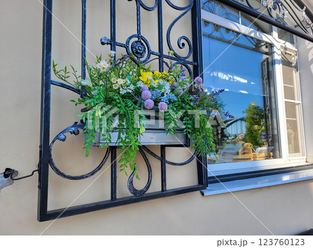 Wooden planter with artificial flowers on a wrought-iron grate by the window. Wooden planter with artificial flowers on a wrought-iron grate by the window. 123760123