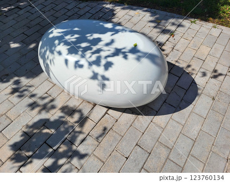 On a beautiful sunny day, a single white decorative concrete oval lies in a shady garden. On a beautiful sunny day, a single white decorative concrete oval lies in a shady garden. 123760134