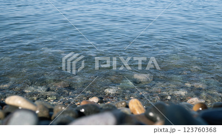 Clear blue water gently washing over smooth, colorful pebbles on a tranquil shoreline 123760368