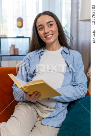 Pregnant Caucasian woman reading book advice child care guide feeling relax on cozy couch at home Pregnant Caucasian woman reading book advice child care guide feeling relax on cozy couch at home 123762582
