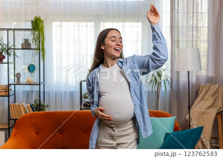 Happy smiling young pregnant woman playfully dancing listening music touching her big belly at home Happy smiling young pregnant woman playfully dancing listening music touching her big belly at home 123762583
