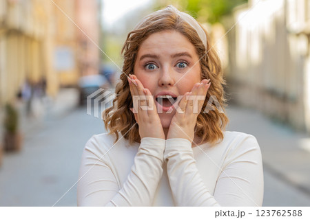 Redhead woman looking surprised at camera shocked by sudden win good victory news wow in city street Redhead woman looking surprised at camera shocked by sudden win good victory news wow in city street 123762588