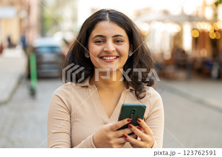 Indian woman use smartphone typing text messages browsing internet finishing work looking at camera Indian woman use smartphone typing text messages browsing internet finishing work looking at camera 123762591