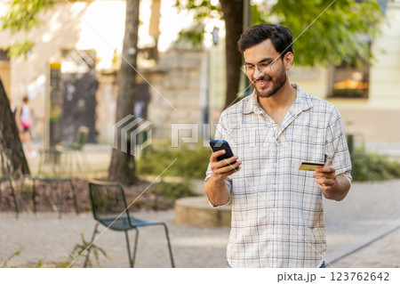 Indian young man using credit card smartphone while transferring money, purchases online outdoors 123762642