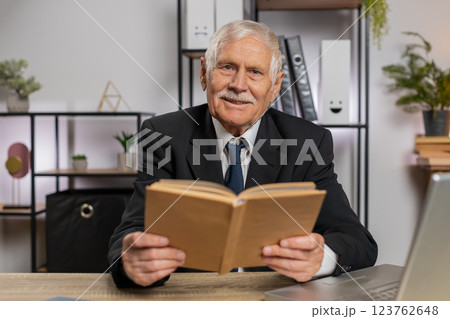 Bored Caucasian senior businessman reading book, literature, taking a rest after work at table 123762648