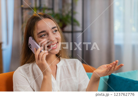 Happy young Caucasian woman making mobile phone conversation with friends sitting on couch at home 123762776