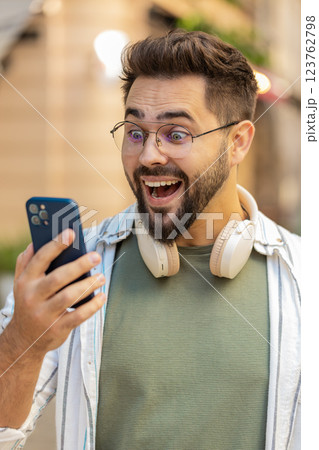 Happy young man using smartphone celebrating victory win good message news on city town street 123762798