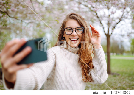 Selfie time. Young woman takes selfie photo in blooming spring park. Concept of relaxation, walking. Selfie time. Young woman takes selfie photo in blooming spring park. Concept of relaxation, walking. 123763007