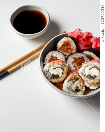 Sushi rolls in a bowl with pink ginger and soy sauce and wooden sticks on white table 123763550