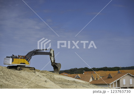 Excavator working on Biscarosse coastline during sunny day with houses in the background Excavator working on Biscarosse coastline during sunny day with houses in the background 123763730