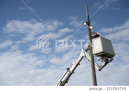 Worker conducts maintenance on a tall light pole using a lift beneath a clear blue sky with 123763738