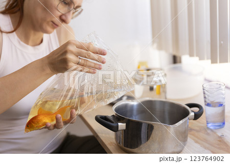 Woman holding plastic bag with goldfish over pot in kitchen 123764902