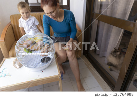 Mother and son feeding a parrot in a cage on the balcony 123764999