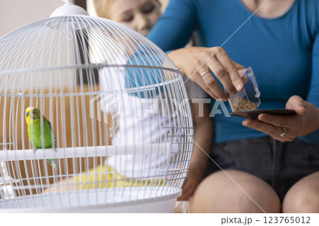 Mother and daughter feeding a green budgie in a cage 123765012