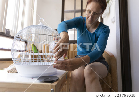Woman changing water in a bird cage with a green parrot 123765019