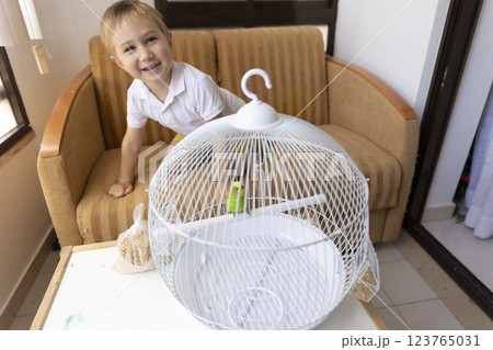 Smiling child playing with green parrot in white cage Smiling child playing with green parrot in white cage 123765031