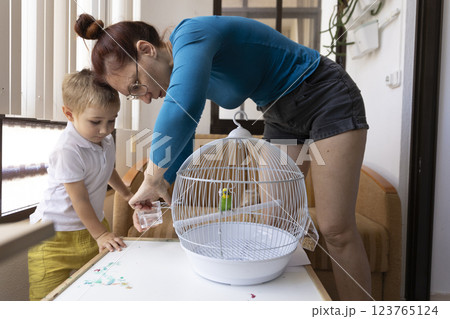 Mother and son changing water in bird cage at home 123765124