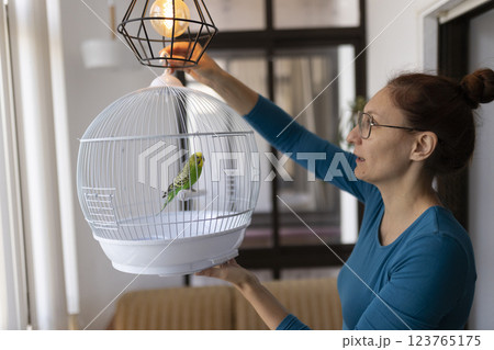 Woman hanging birdcage with a budgie near a lamp 123765175