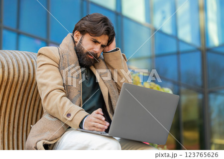 Indian young man using laptop browsing loses lottery results, bad news sitting in city street Indian young man using laptop browsing loses lottery results, bad news sitting in city street 123765626
