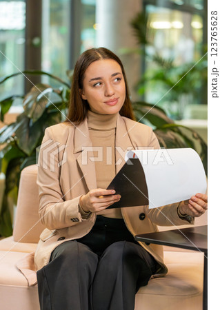 Caucasian young female entrepreneur in formal analyzing graph documents reports in office lobby Caucasian young female entrepreneur in formal analyzing graph documents reports in office lobby 123765628
