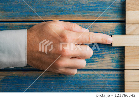 Hand of caucasian businessman pushing a wooden peg into a stack of them Hand of caucasian businessman pushing a wooden peg into a stack of them 123766342