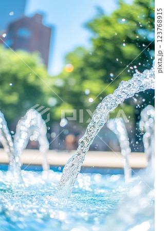 Clear water fountain arcs sparkle in sunlight against green trees and blue sky. 123768915