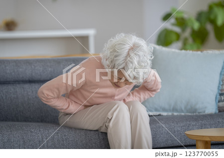 ソファに座り下腹部をおさえて苦しむシニア女性 ソファに座り下腹部をおさえて苦しむシニア女性 123770055