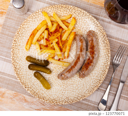 Fried sausages with served with french fries potatoes and marinated cucumbers closeup 123770071
