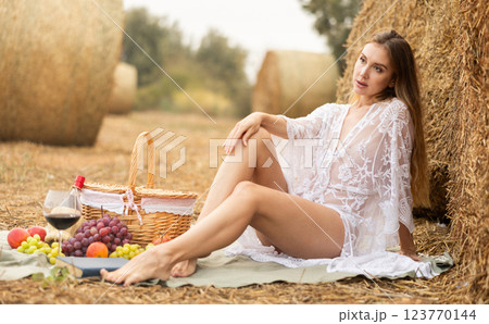 Woman in transparent dress and white lingerie posing at picnic near bale of hay Woman in transparent dress and white lingerie posing at picnic near bale of hay 123770144