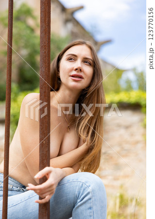 Portrait of half-naked young woman on city street near wrought iron fence 123770156